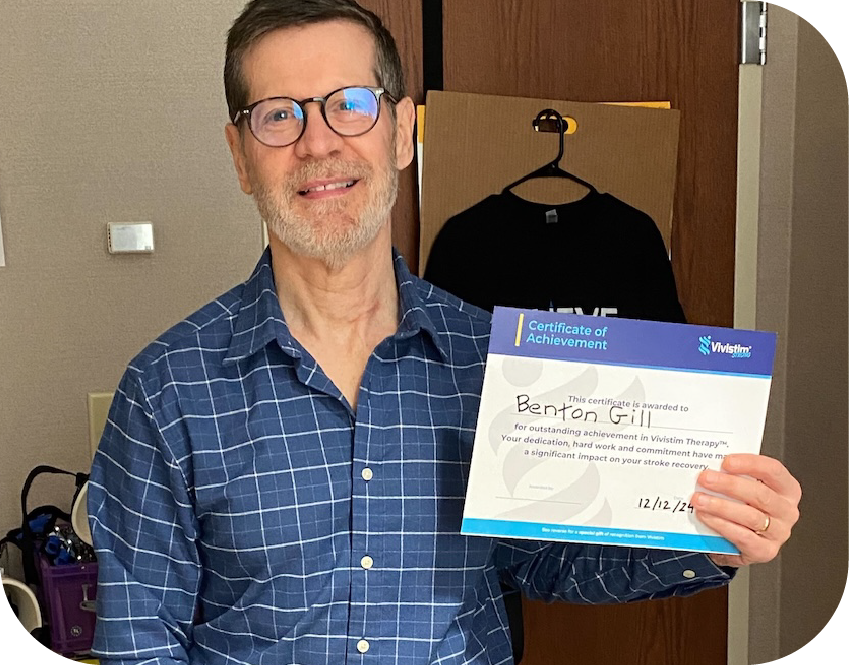 Man with glasses and a beard standing indoors and holding a Certificate of Achievement.