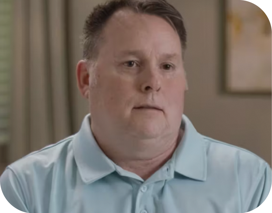 Man with short brown hair wearing a light blue polo shirt, sitting indoors with a neutral expression.