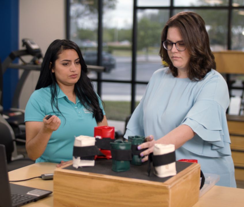Occupational therapist guiding a patient through a rehabilitation exercise using weighted wrist cuffs in a therapy clinic